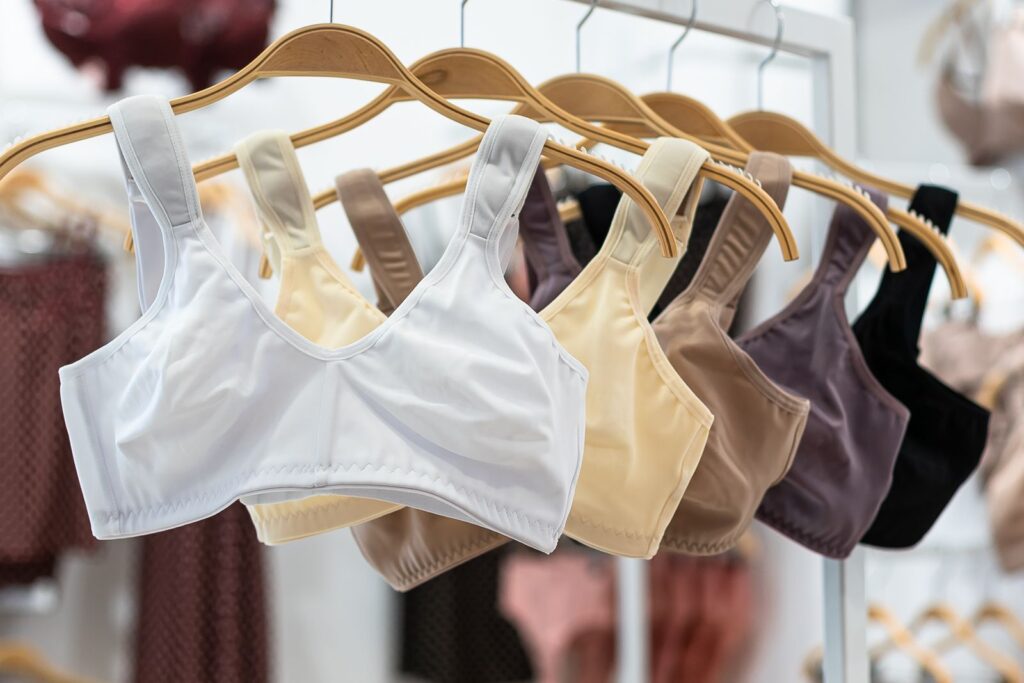 Bløde bh'er uden bøjle med brede stropper i hvid, beige, brun, lilla og sort på træbøjler i en undertøjsbutik