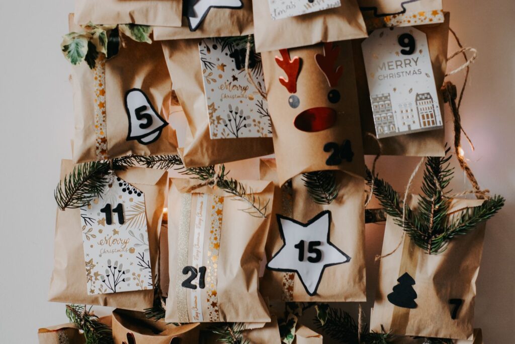 Pakkekalender af brune papirposer med tal, julemærker og grangrene hængt op på en lys væg