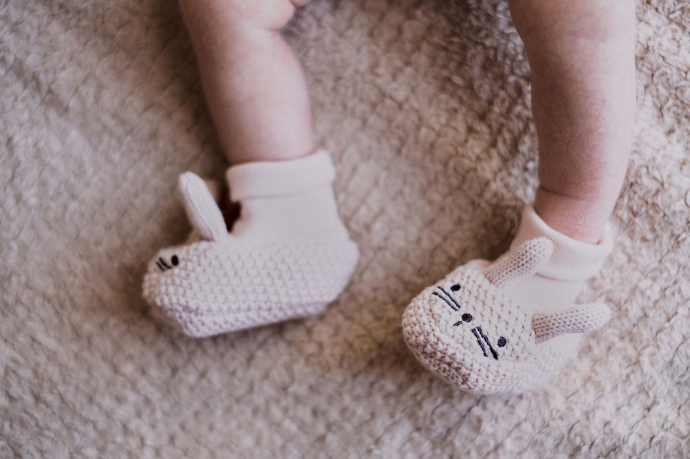 Nyfødt baby med strikkede, lyse futter formet som kaniner på et blødt tæppe